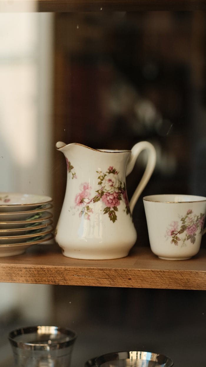 A vintage floral ceramic jug and cup on a wooden shelf, creating an elegant still life composition.